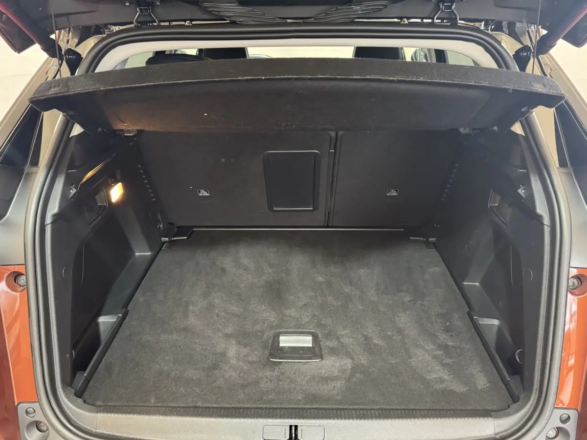Coffre ouvert vu de l’arrière d’un Peugeot 3008 orange, espace de chargement propre avec cache-bagages déployé.