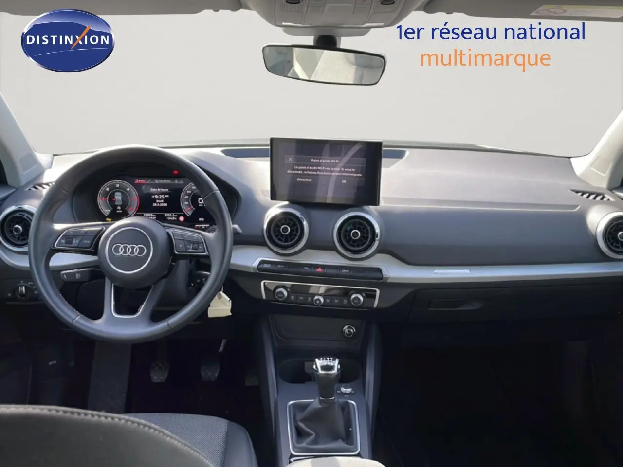 Vue intérieure avant de l'Audi Q2 30 TDI S-Line 2025, tableau de bord noir avec écran central et volant cuir multifonction.