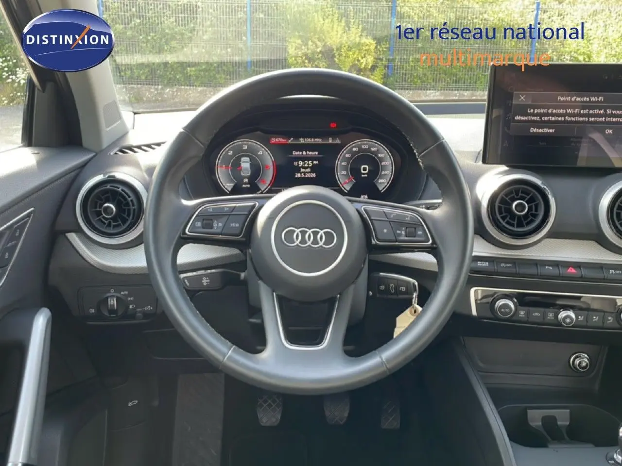 Vue intérieure frontale du volant cuir noir d’un Audi Q2 gris Manhattan, avec tableau de bord digital et écran tactile central.