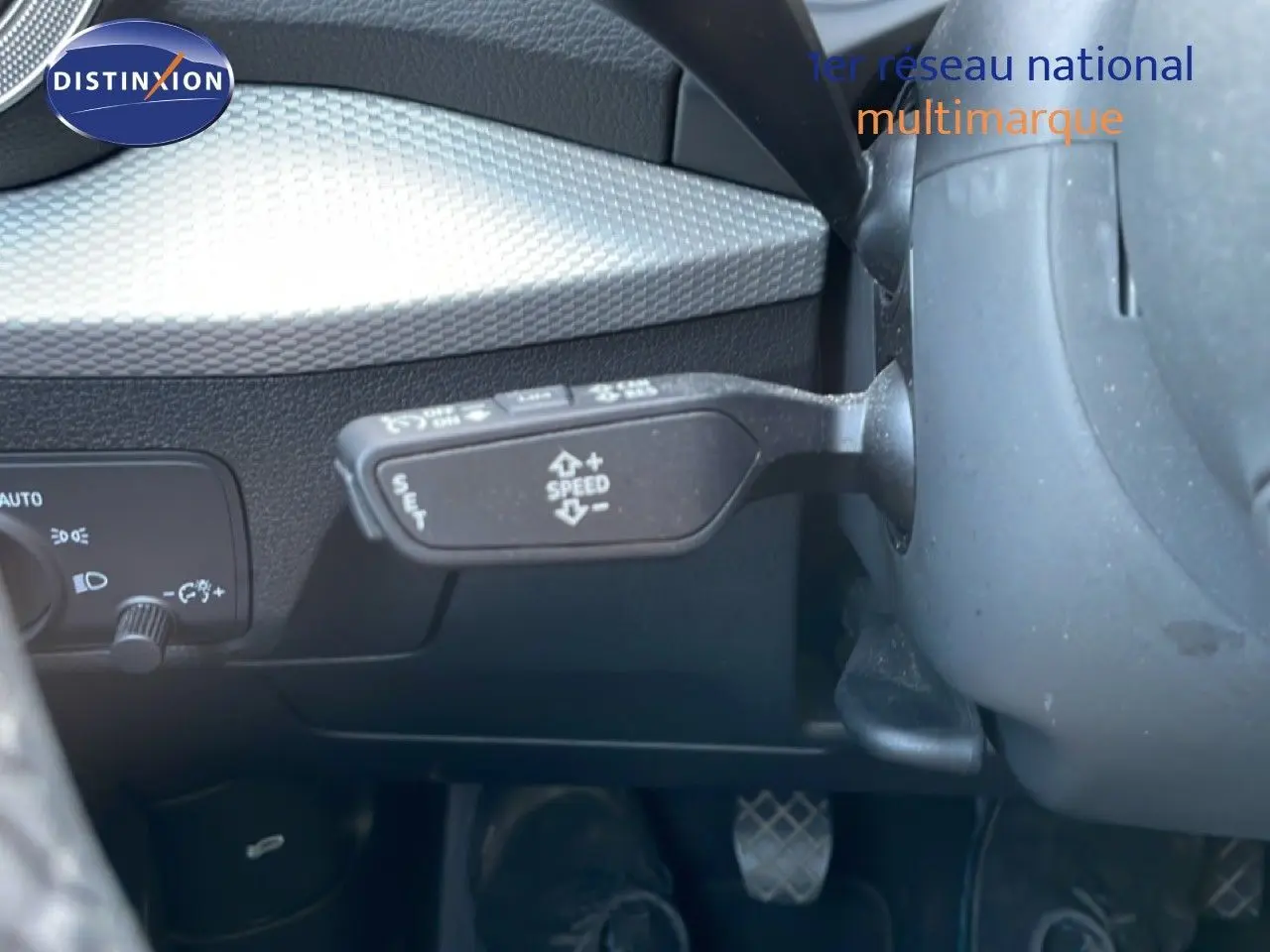 Gros plan sur la commande de régulateur de vitesse à gauche du volant dans l’Audi Q2 gris Manhattan 2025.