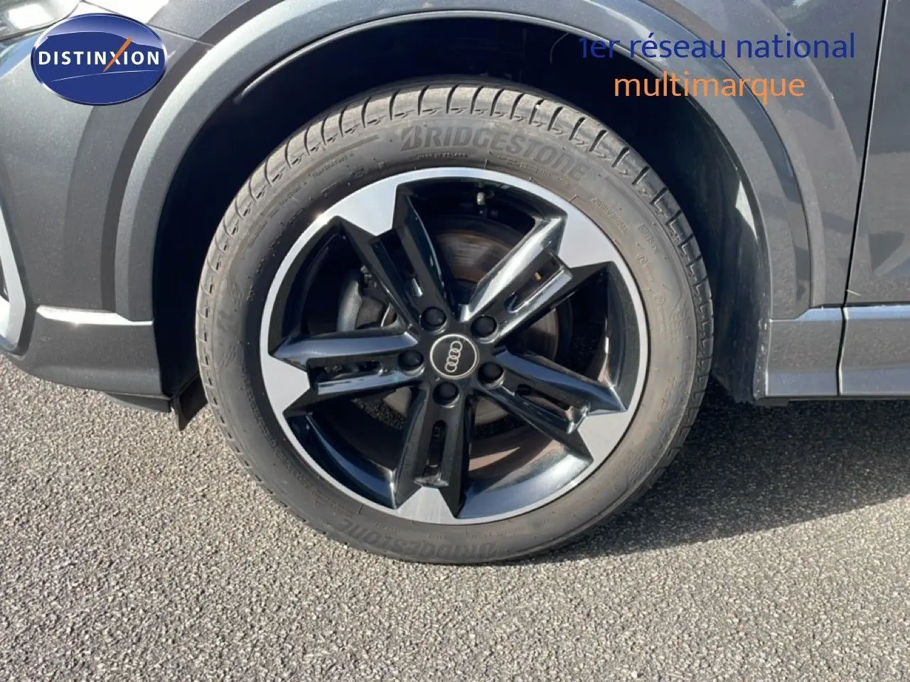 Gros plan sur la roue avant droite d’un Audi Q2 gris Manhattan avec jante alliage bicolore et pneu Bridgestone.