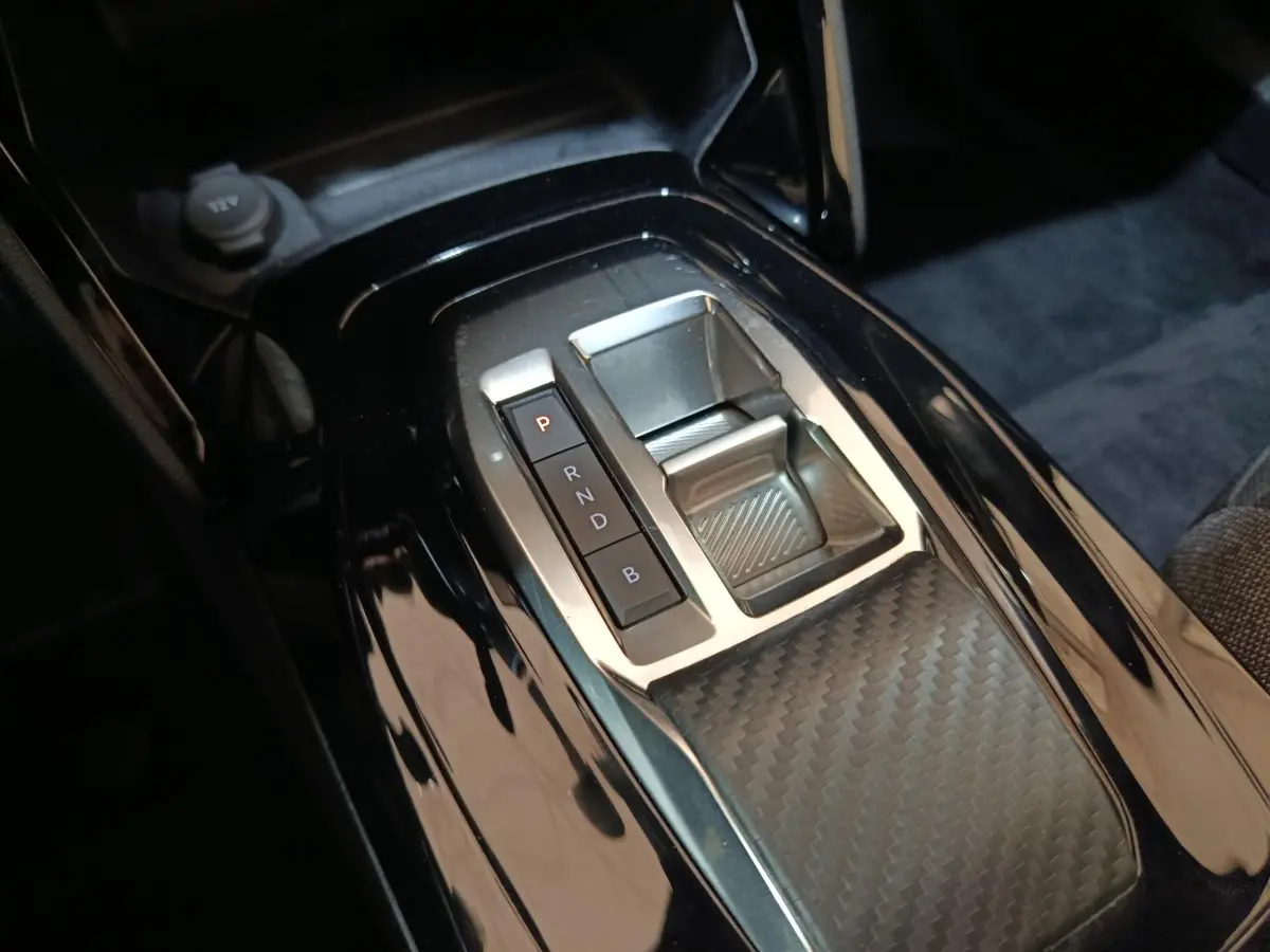 Gros plan sur la console centrale noire brillante avec sélecteur de vitesses électrique du Peugeot E-2008 gris clair.