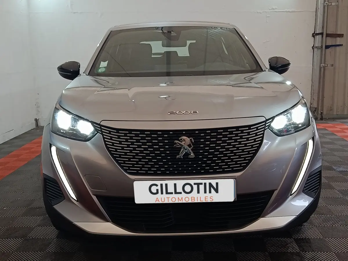 Vue frontale d'un Peugeot E-2008 électrique gris clair avec phares LED allumés et calandre noire distinctive.