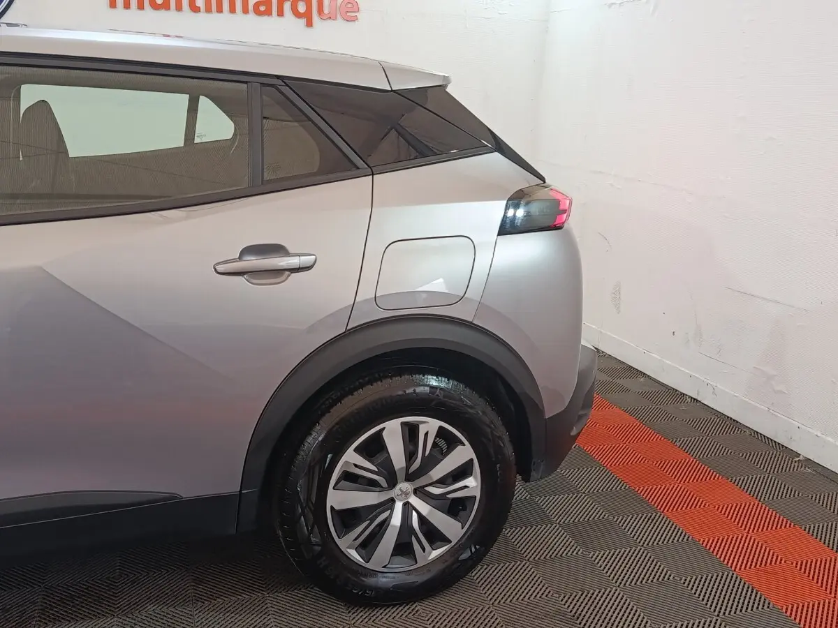 Vue arrière côté droit du Peugeot E-2008 électrique gris clair, mettant en valeur la roue et le port de charge.