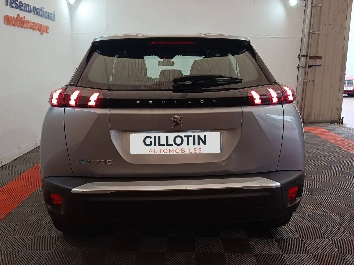 Vue arrière d’un Peugeot E-2008 électrique gris clair avec feux LED allumés en intérieur showroom.