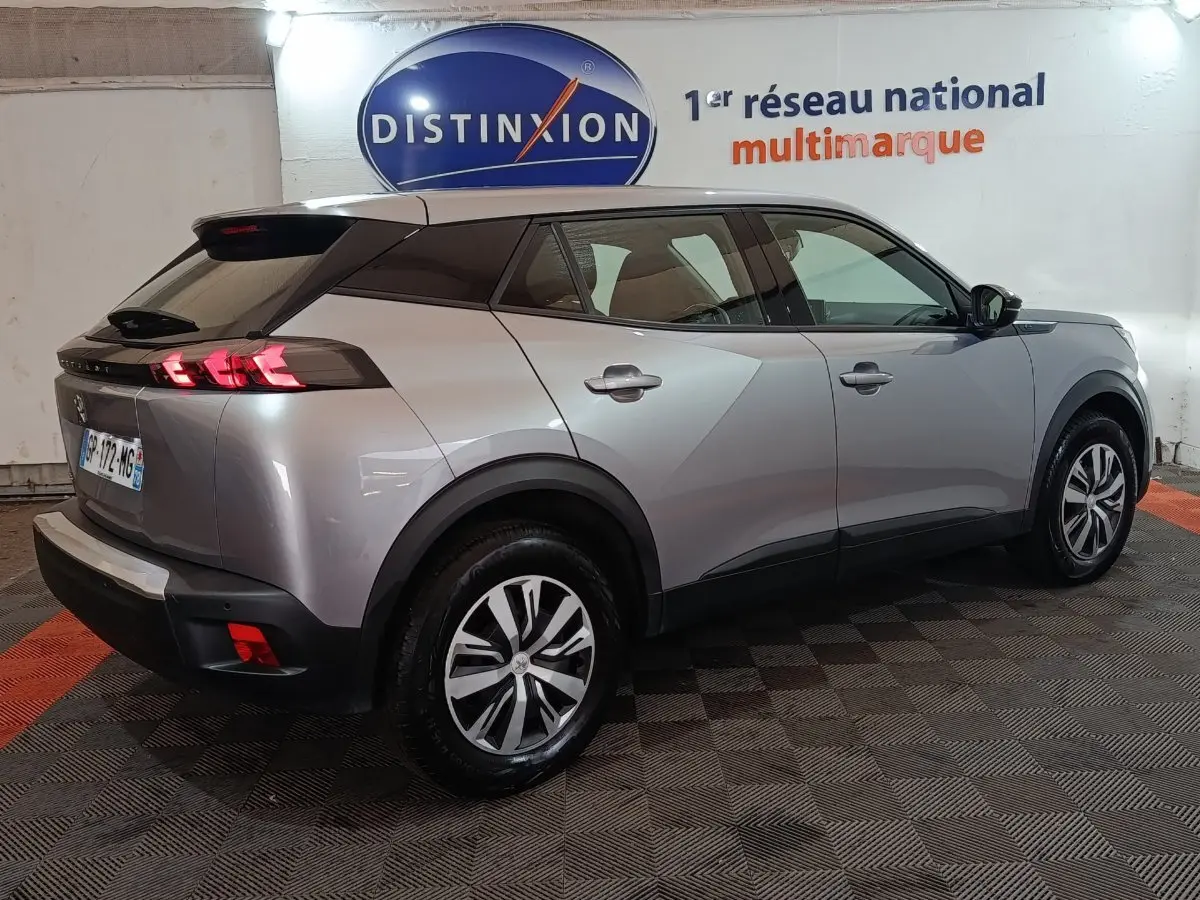 Peugeot E-2008 électrique gris clair vue 3/4 arrière droit, feux LED et jantes alliage distinctives visibles.