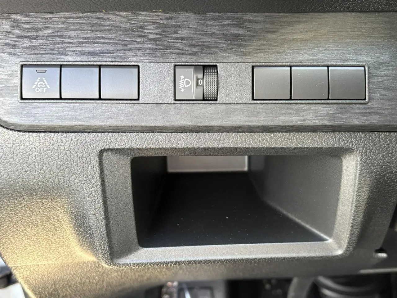 Gros plan sur les commandes noires du tableau de bord de l'Opel Vivaro blanc, avec bouton de réglage des phares et espace de rangement.