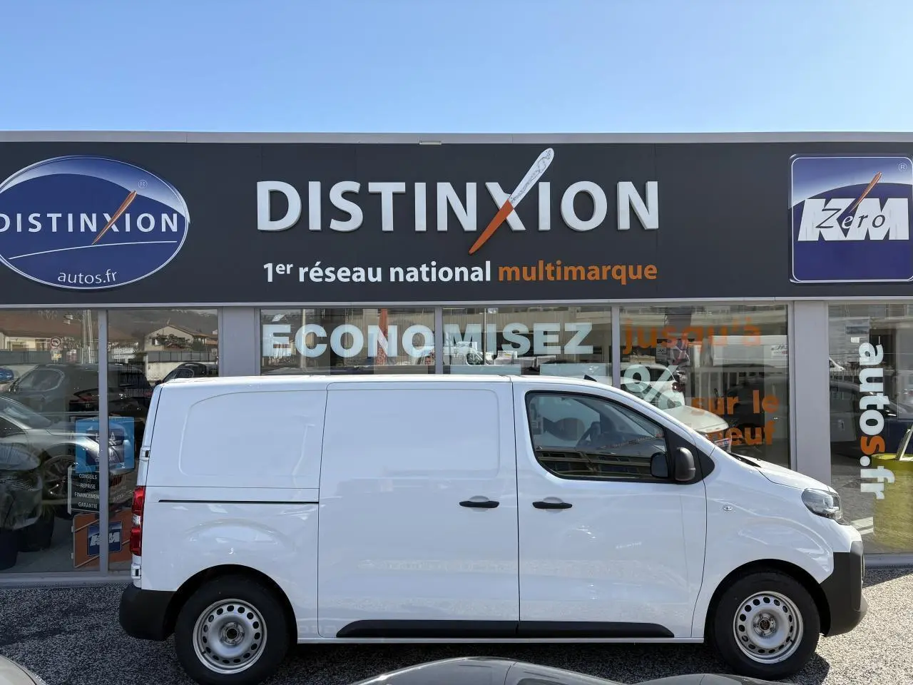 Profil latéral droit d'un utilitaire Opel Vivaro blanc 2024 garé devant une concession Distinxion.
