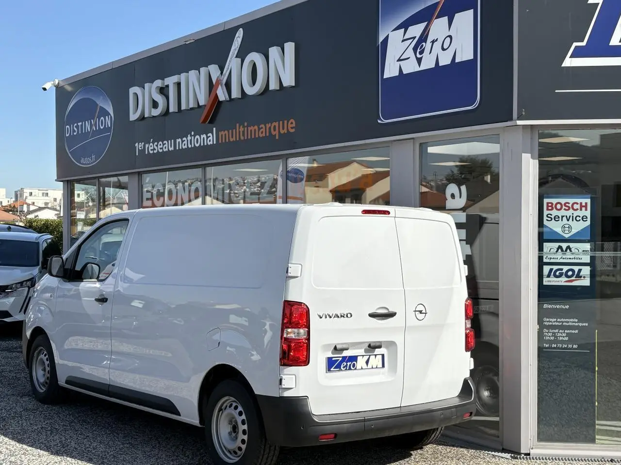 Vue 3/4 arrière droite d'un utilitaire Opel Vivaro blanc stationné devant un garage multimarque.