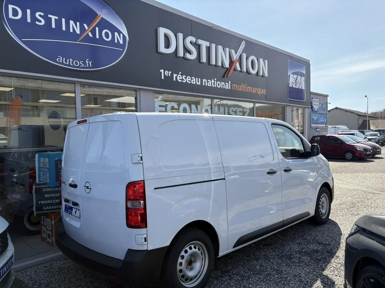 Vue 3/4 arrière droite d’un utilitaire Opel Vivaro blanc stationné devant un concessionnaire Distinxion.