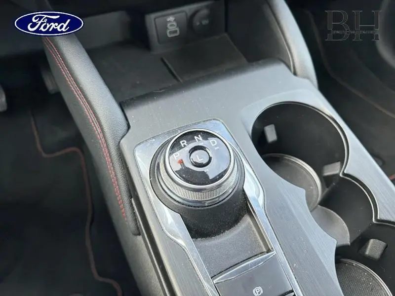 Gros plan sur la molette de sélection de la boîte automatique du Ford Kuga gris, avec accoudoir et porte-gobelets visibles.