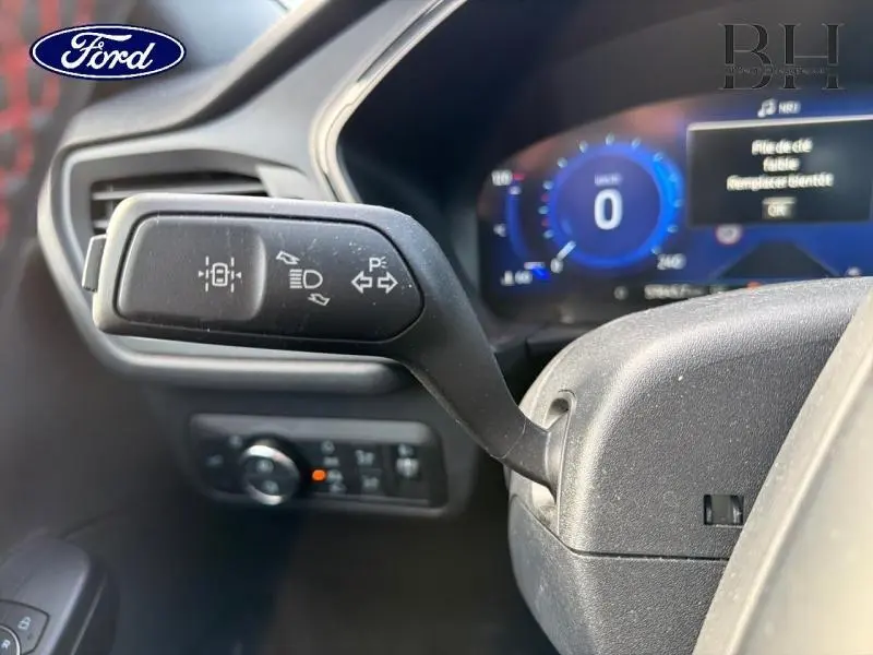 Gros plan sur la manette de clignotants noire à l'intérieur d'un Ford Kuga 2023, tableau de bord numérique en arrière-plan.