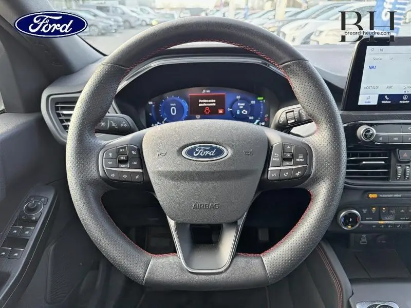 Vue frontale du volant cuir perforé avec surpiqûres rouges du Ford Kuga 2023, tableau de bord numérique et écran tactile visibles.