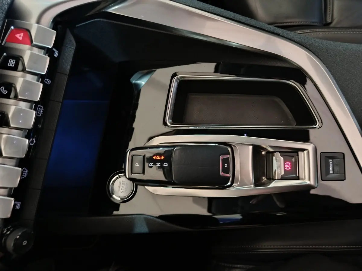 Vue plongeante sur la console centrale noire brillante du Peugeot 3008 blanc, avec levier de vitesse automatique et bouton start.