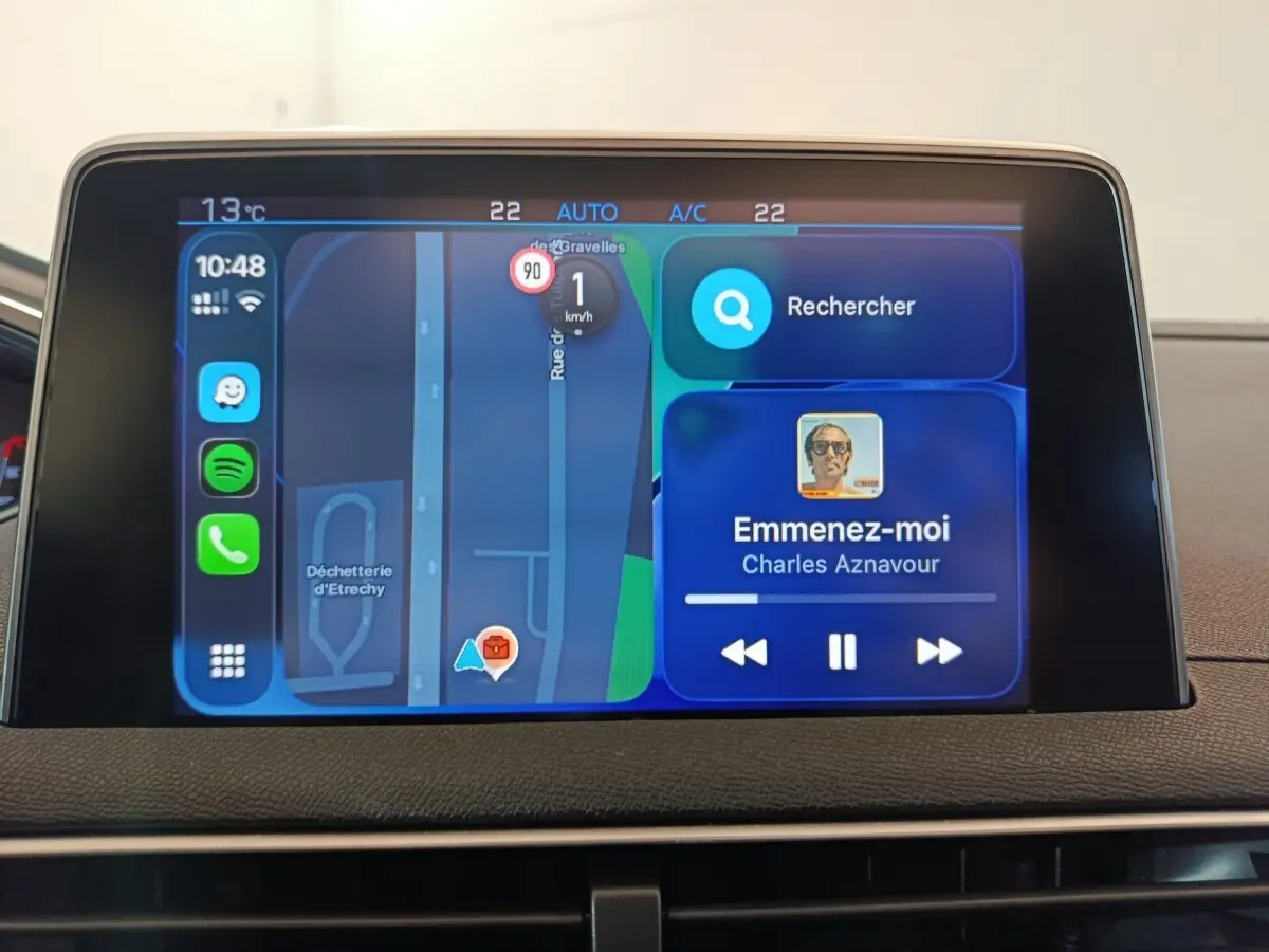 Écran tactile central du tableau de bord du Peugeot 3008 blanc, affichant navigation et musique en cours.