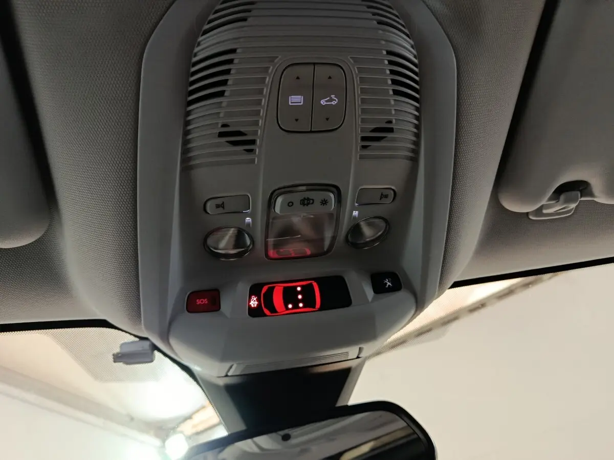 Vue en contre-plongée du plafonnier intérieur gris avec commandes lumineuses et bouton SOS du Peugeot 3008 blanc.