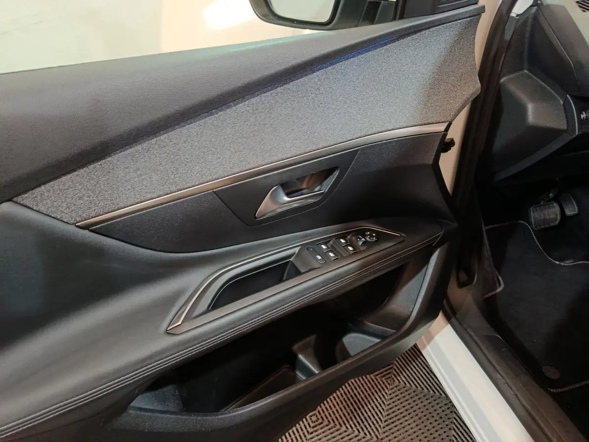 Vue intérieure côté conducteur de la porte d’un Peugeot 3008 blanc, avec commandes électriques et garniture textile grise.