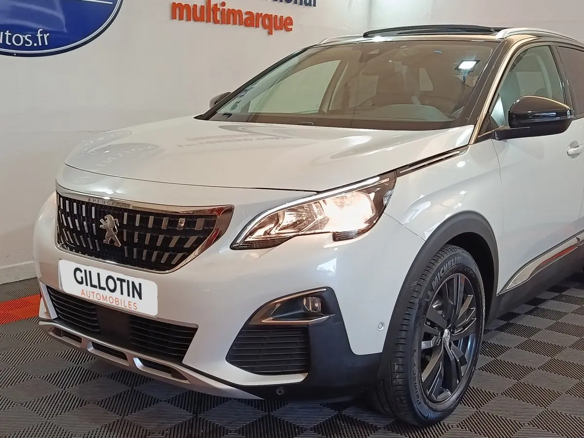 Vue 3/4 avant droit d’un Peugeot 3008 blanc de 2019 avec calandre noire et phares allumés en intérieur showroom.