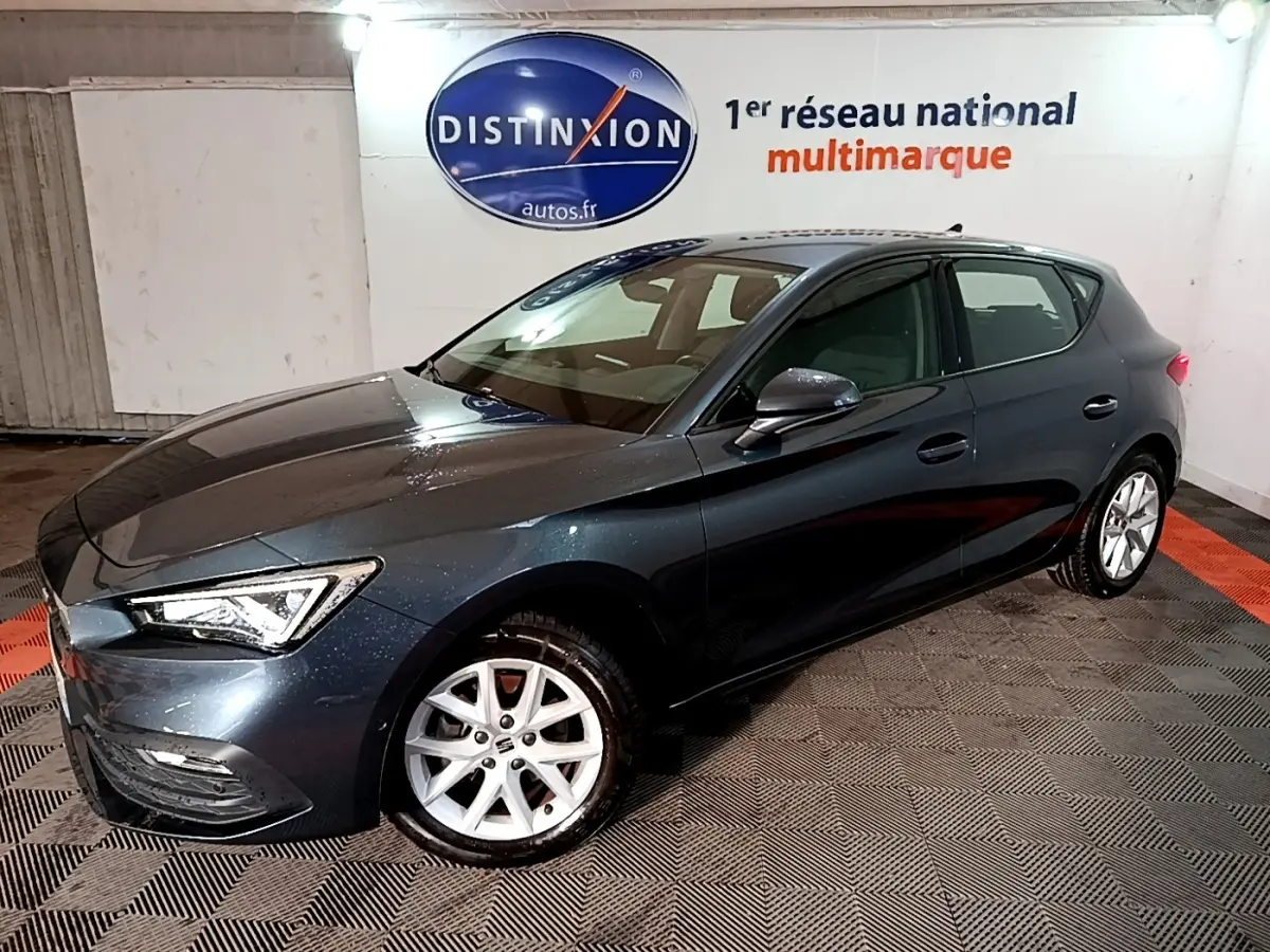 Vue 3/4 avant droit d'une SEAT Leon gris clair 2023 avec jantes alliage et phares LED ellipsoïdaux.