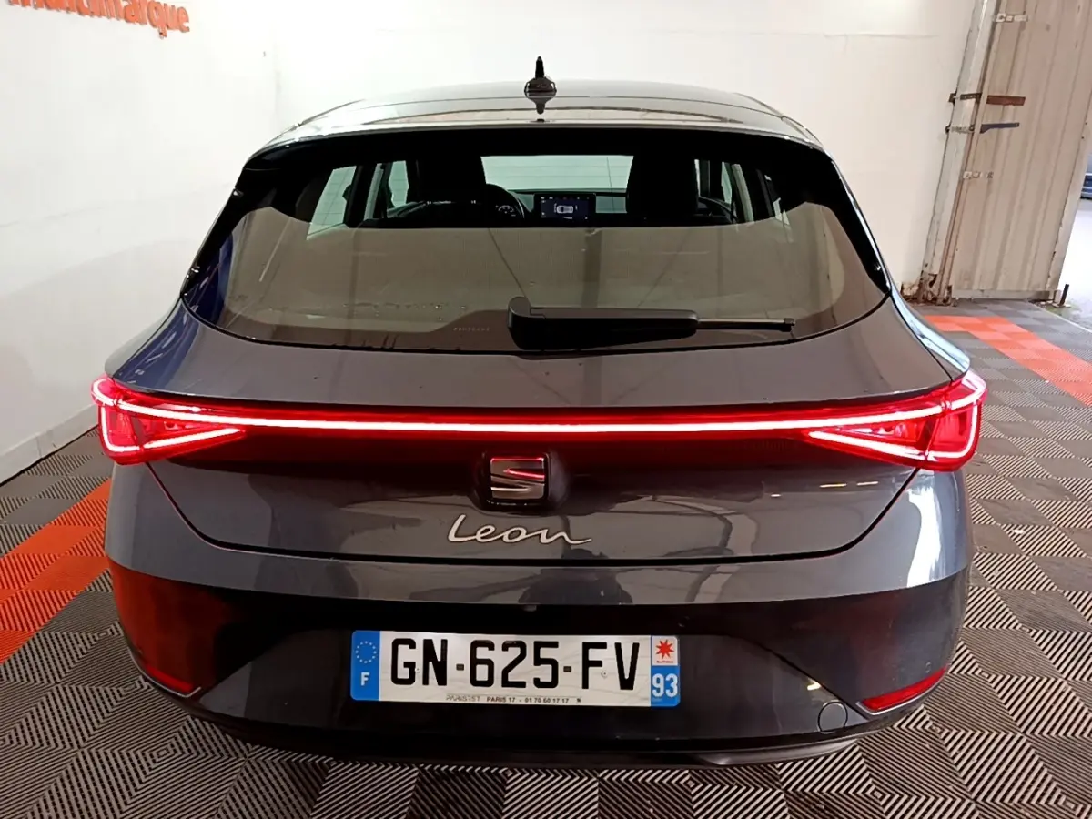Vue arrière d'une SEAT Leon gris clair 2023 avec feux arrière LED allumés en bande continue rouge.