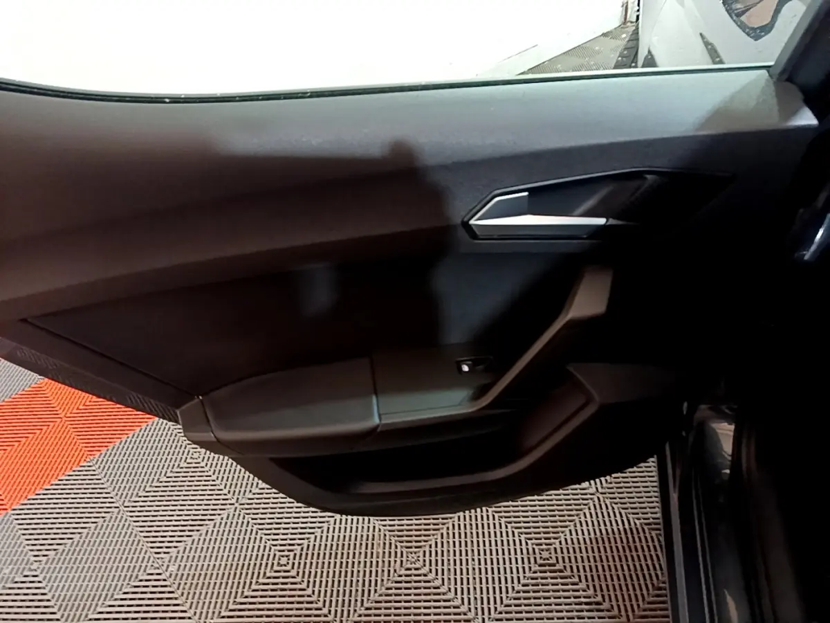 Vue intérieure sur la porte avant droite noire du SEAT Leon 2023, avec poignée argentée et commande de vitre électrique.