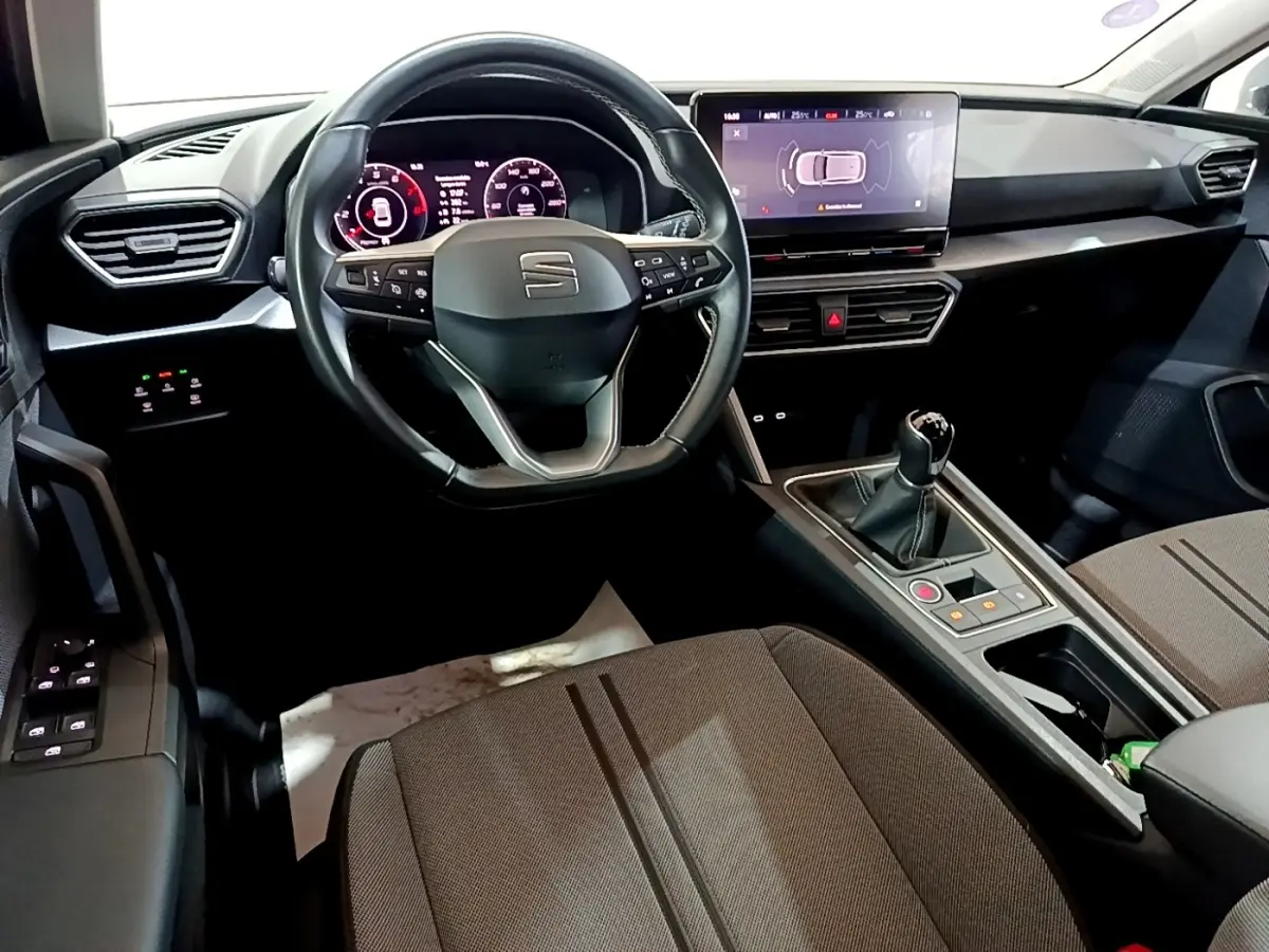 Vue intérieure avant du tableau de bord et volant cuir SEAT Leon 2023 avec écran tactile et boîte manuelle.