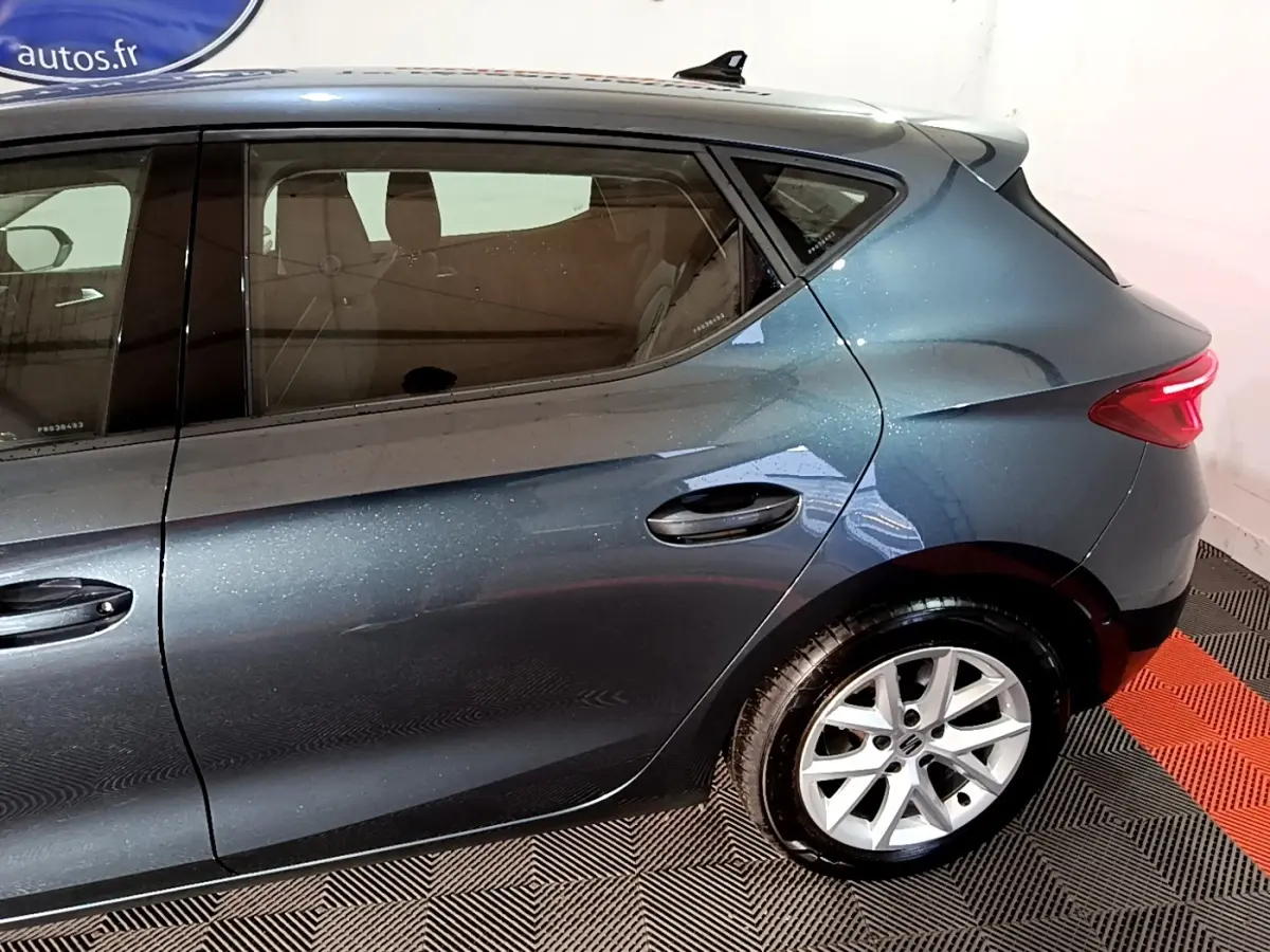 Vue côté droit arrière d'une SEAT Leon gris clair métallisé avec jantes alliage et feux arrière allumés.