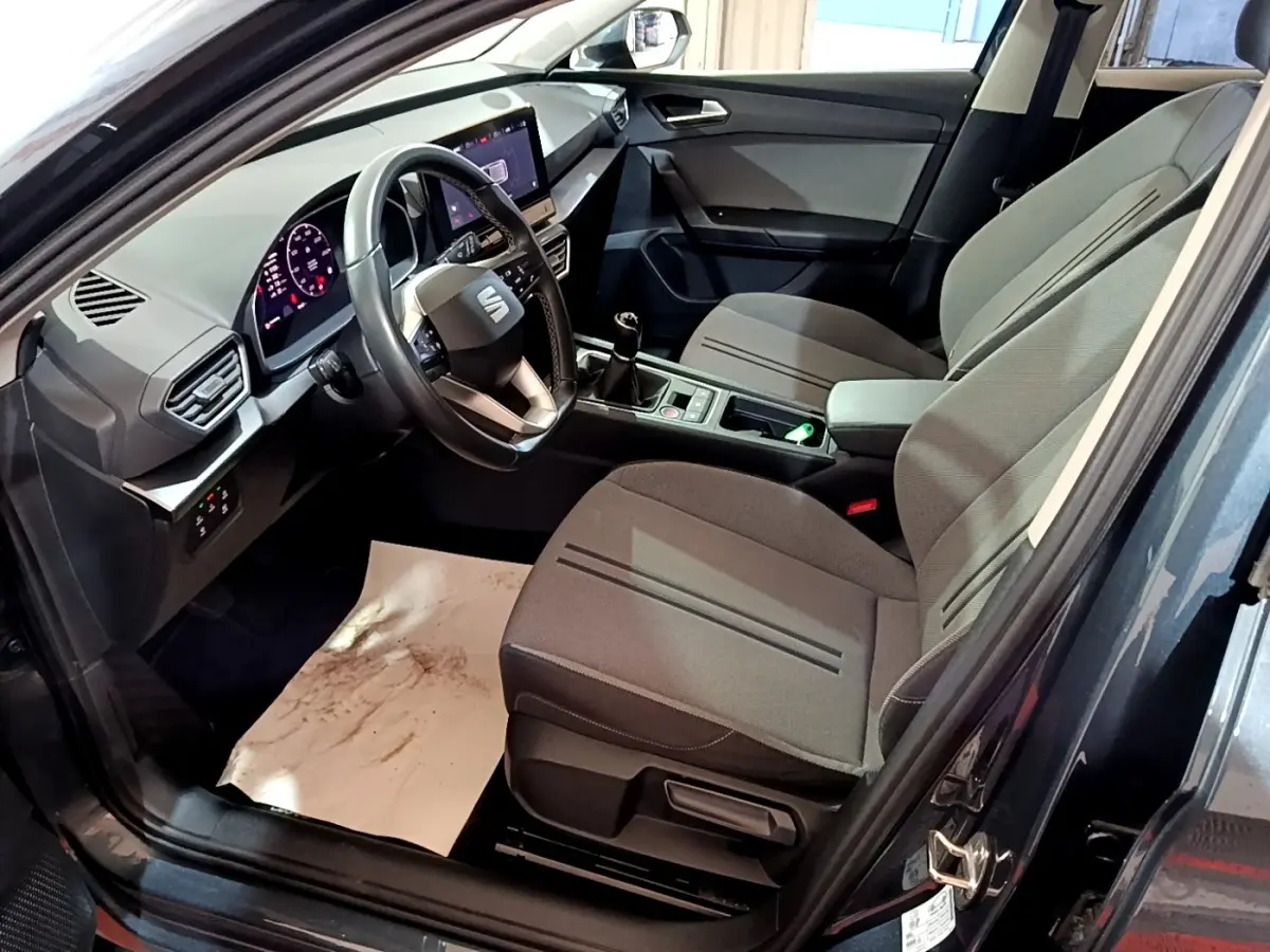 Intérieur de la SEAT Leon 2023 vu côté conducteur, sièges gris, volant cuir, écran tactile et boîte manuelle.
