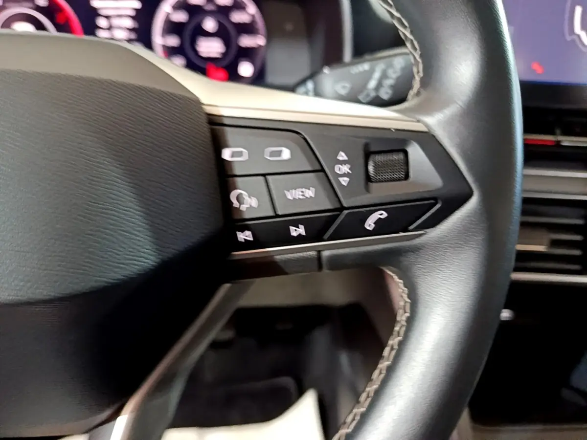 Gros plan sur les commandes gauche du volant cuir du SEAT Leon 2023, avec tableau de bord numérique en arrière-plan.