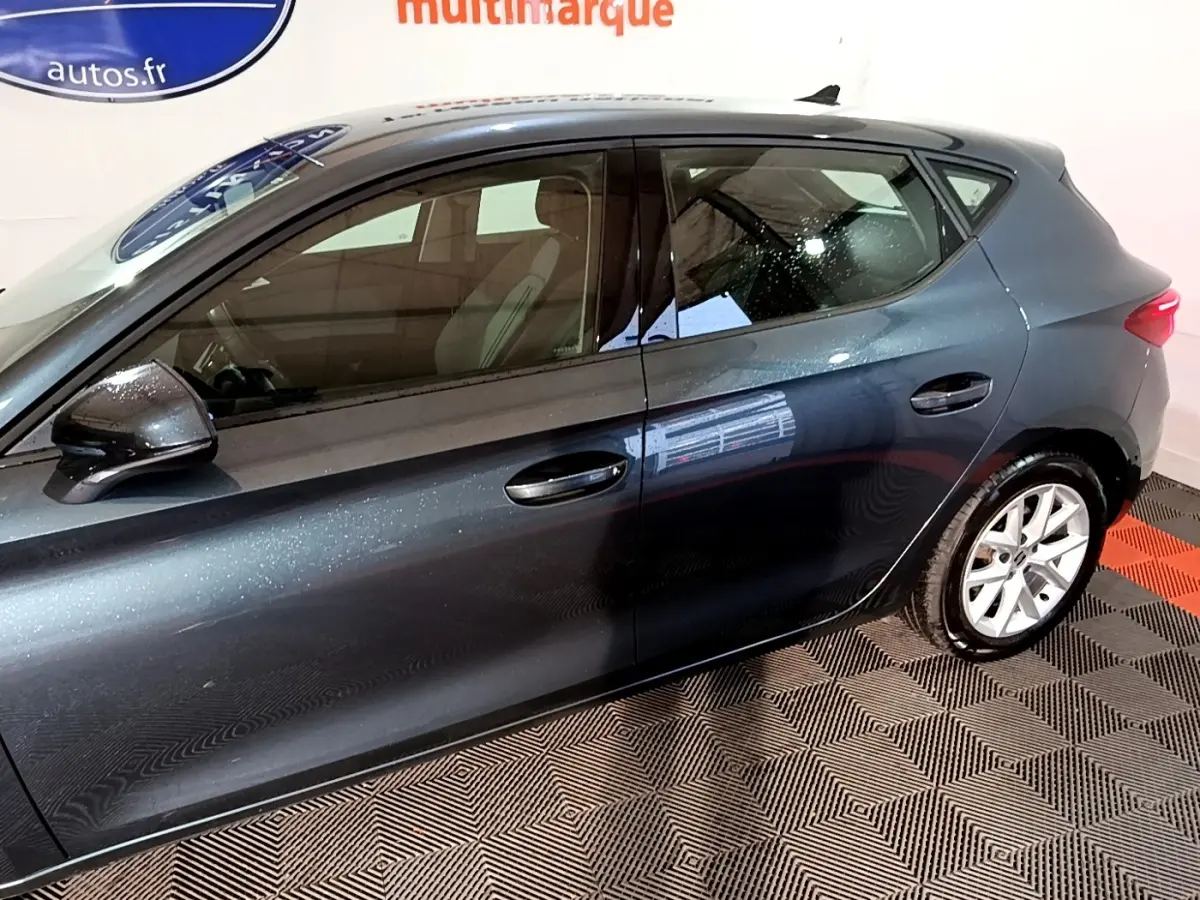 Vue latérale droite d'une SEAT Leon gris clair 2023 avec jantes alliage et rétroviseurs noirs brillants.