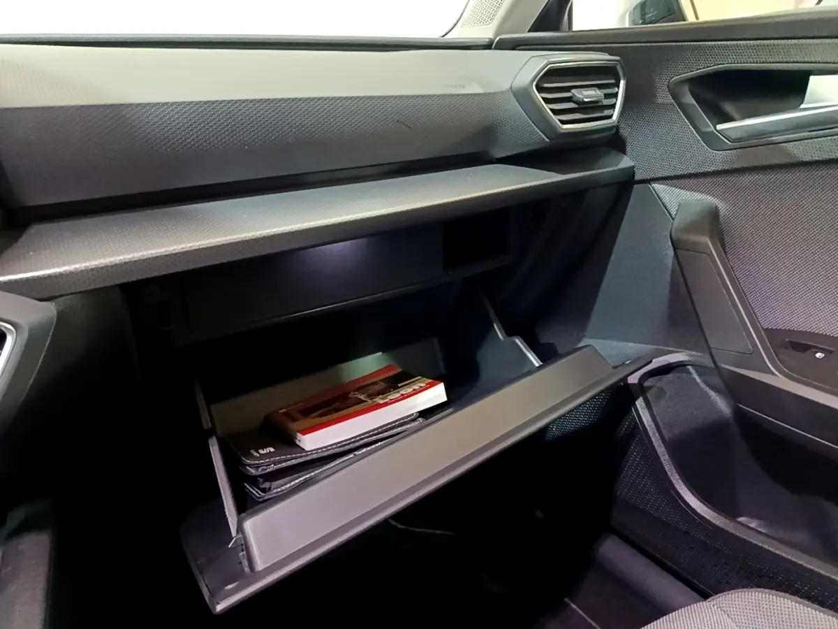 Gros plan sur la boîte à gants ouverte côté passager du SEAT Leon 2023, intérieur noir avec textures modernes.