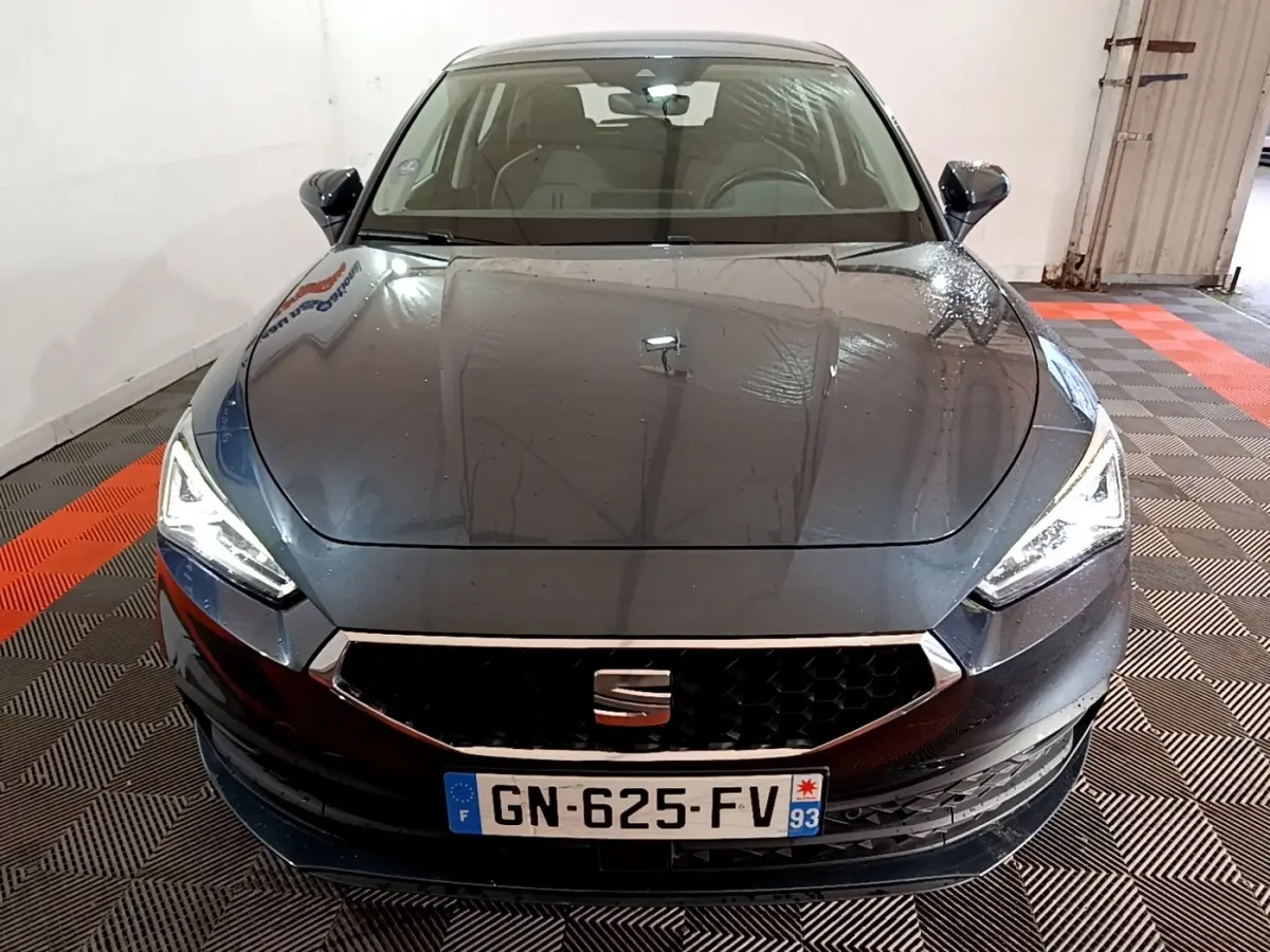 Vue avant d'une SEAT Leon gris clair 2023 avec phares LED allumés dans un garage fermé.