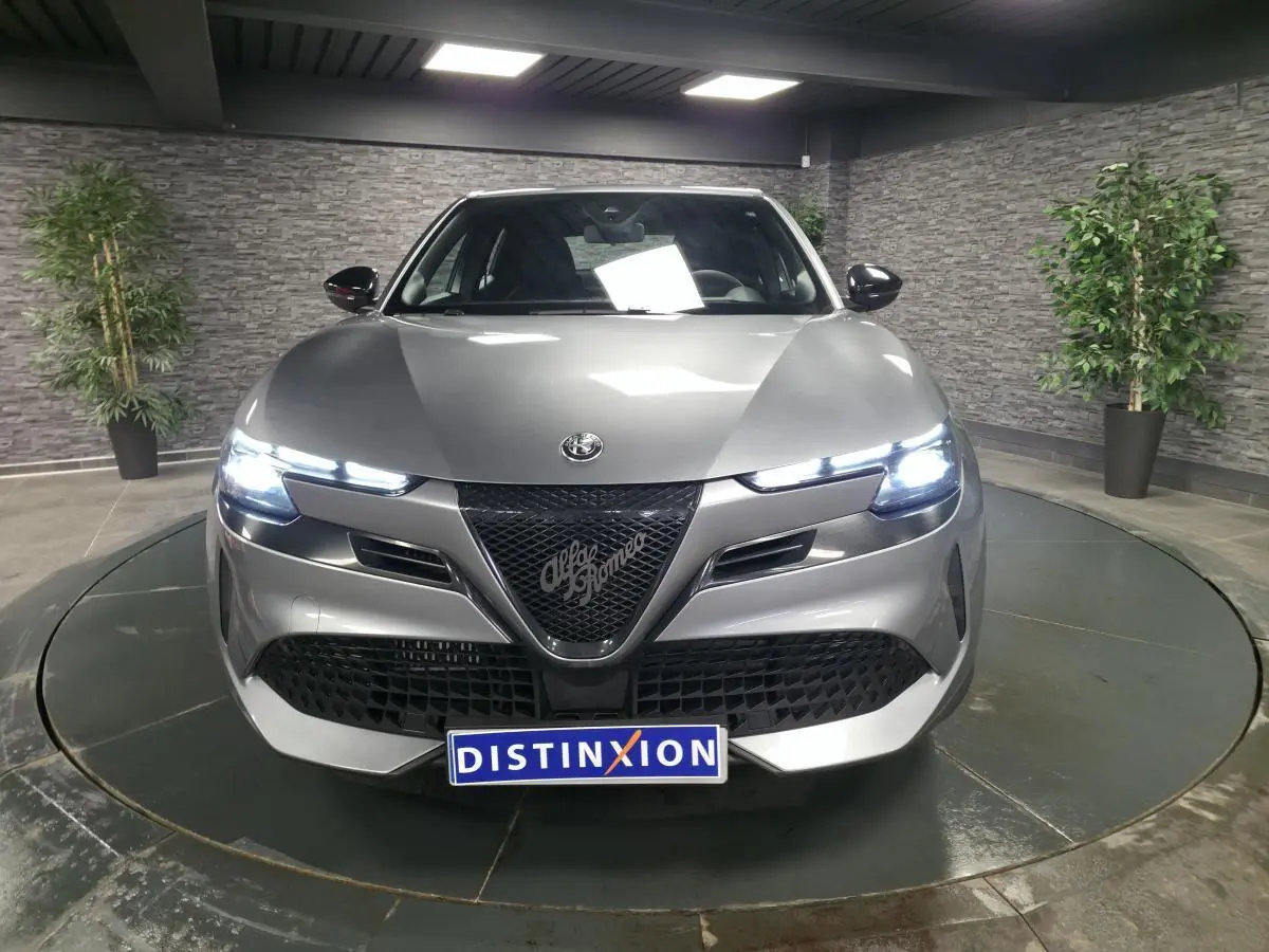 Vue avant d'une Alfa Romeo Junior 1.2 Ibrida gris métallisé avec calandre noire et feux LED allumés.