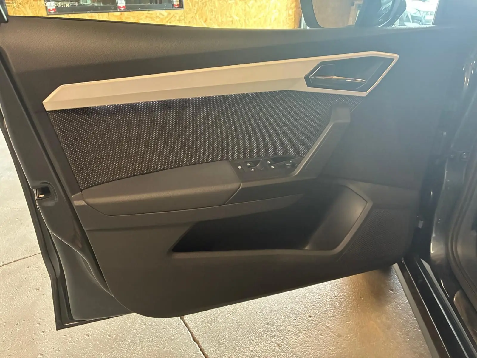 Vue intérieure de la porte avant gauche d'une SEAT Arona gris foncé, avec commandes de vitres et poignée intégrée.