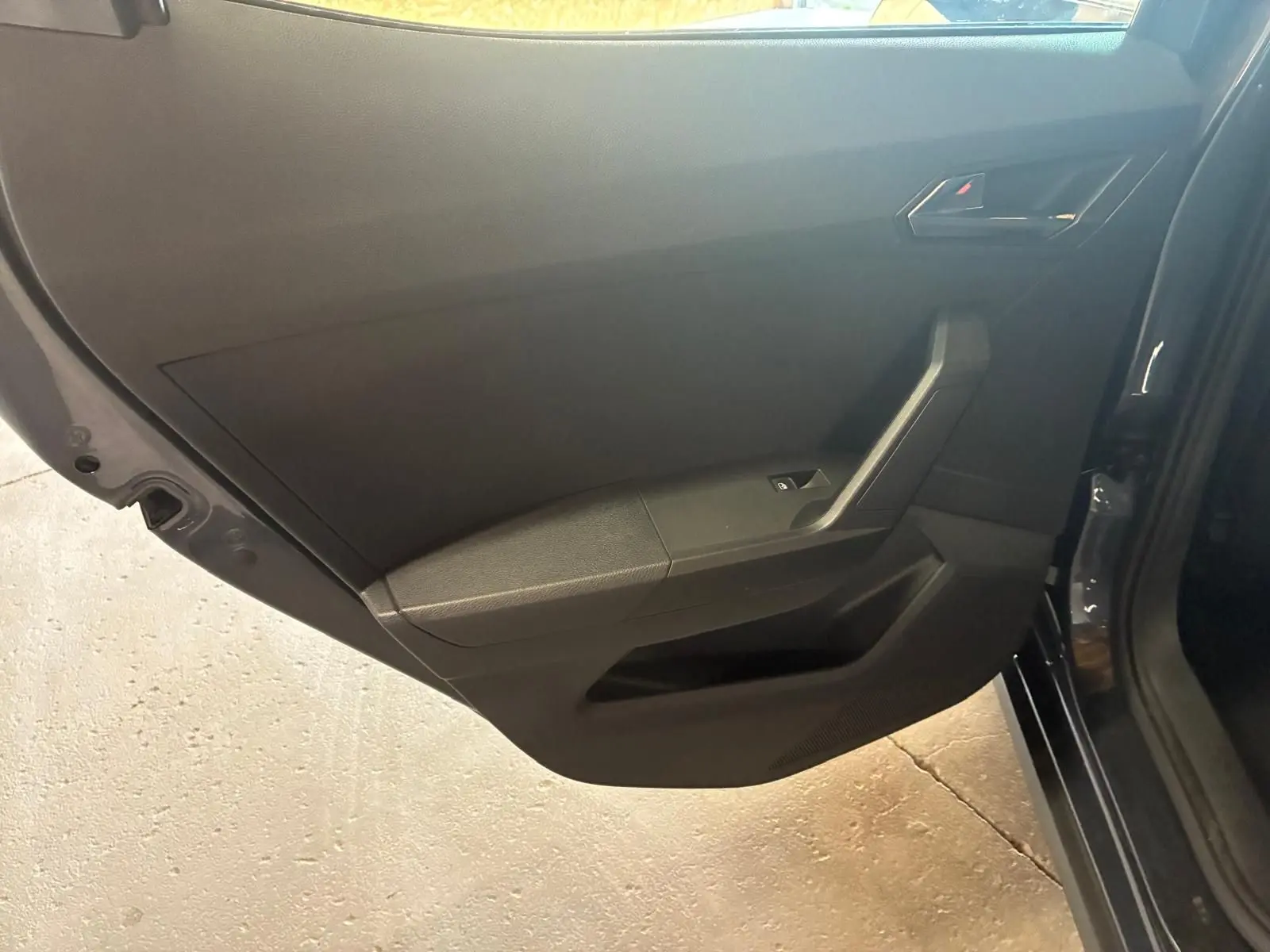 Vue rapprochée de la porte arrière droite intérieure d'un SEAT Arona gris foncé, avec panneau noir et commande de fenêtre.