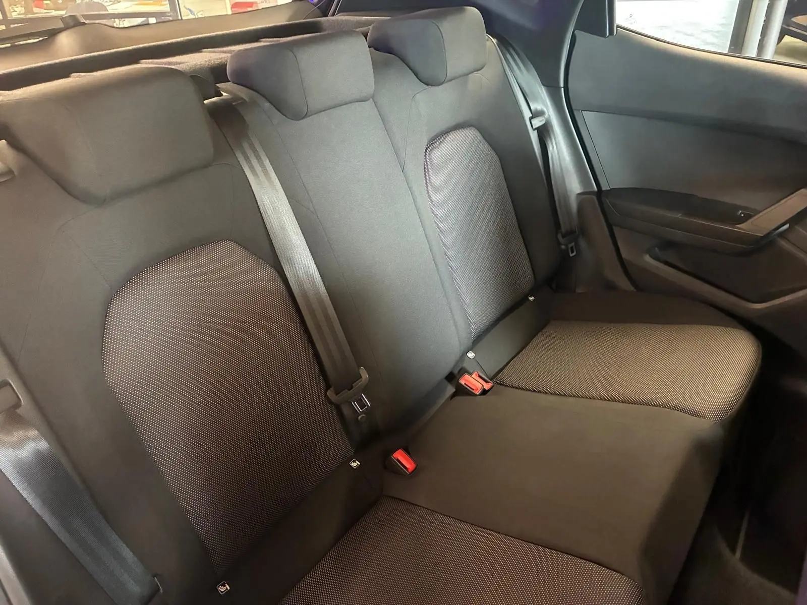 Vue intérieure sur les sièges arrière en tissu noir du SEAT Arona 1.0 TSI 110 XCELLENCE, avec ceintures de sécurité visibles.