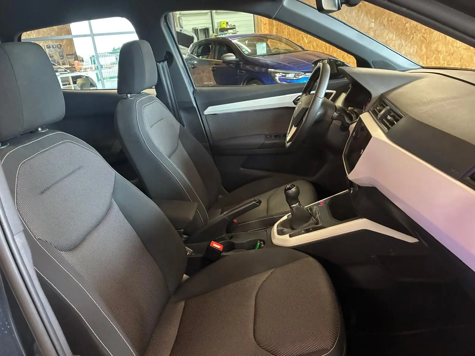 Vue intérieure côté conducteur du SEAT Arona gris foncé 2021, mettant en valeur les sièges tissu noirs et la boîte manuelle.