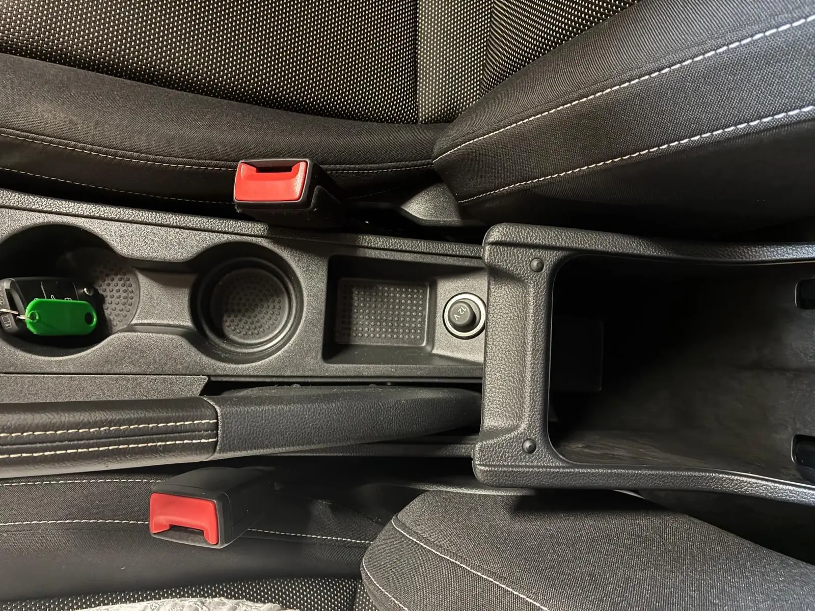 Vue plongeante sur la console centrale noire en tissu du SEAT Arona gris foncé, avec porte-gobelets et accoudoir ouvert.
