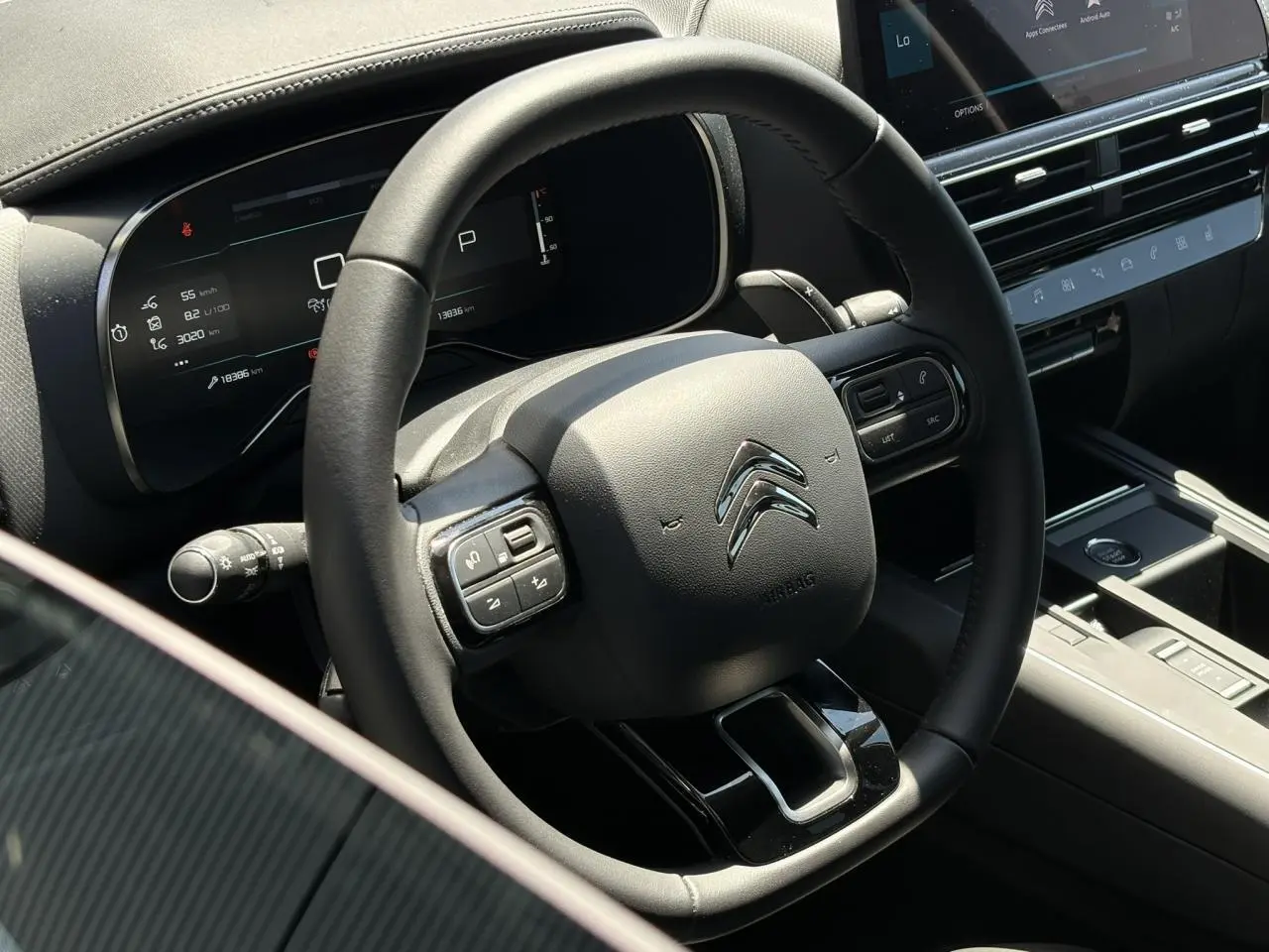 Vue rapprochée du volant noir cuir du Citroën C5 Aircross Hybrid 2025 avec commandes intégrées et tableau de bord numérique.