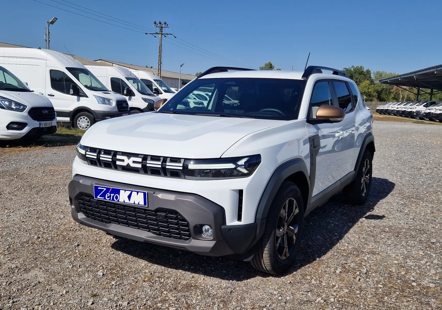 Vue 3/4 avant droite d'un Dacia Duster blanc 2026 avec rétroviseurs bronze et calandre moderne.