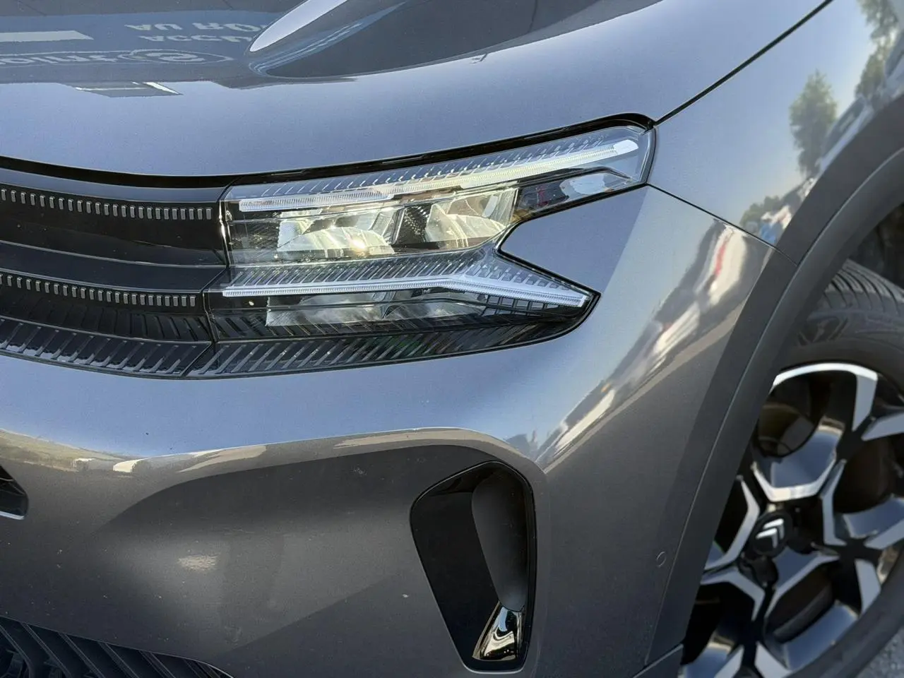 Gros plan sur l'avant droit gris Platinium du Citroën C5 Aircross Hybrid 2025 avec phare LED et jante alliage bi-ton.