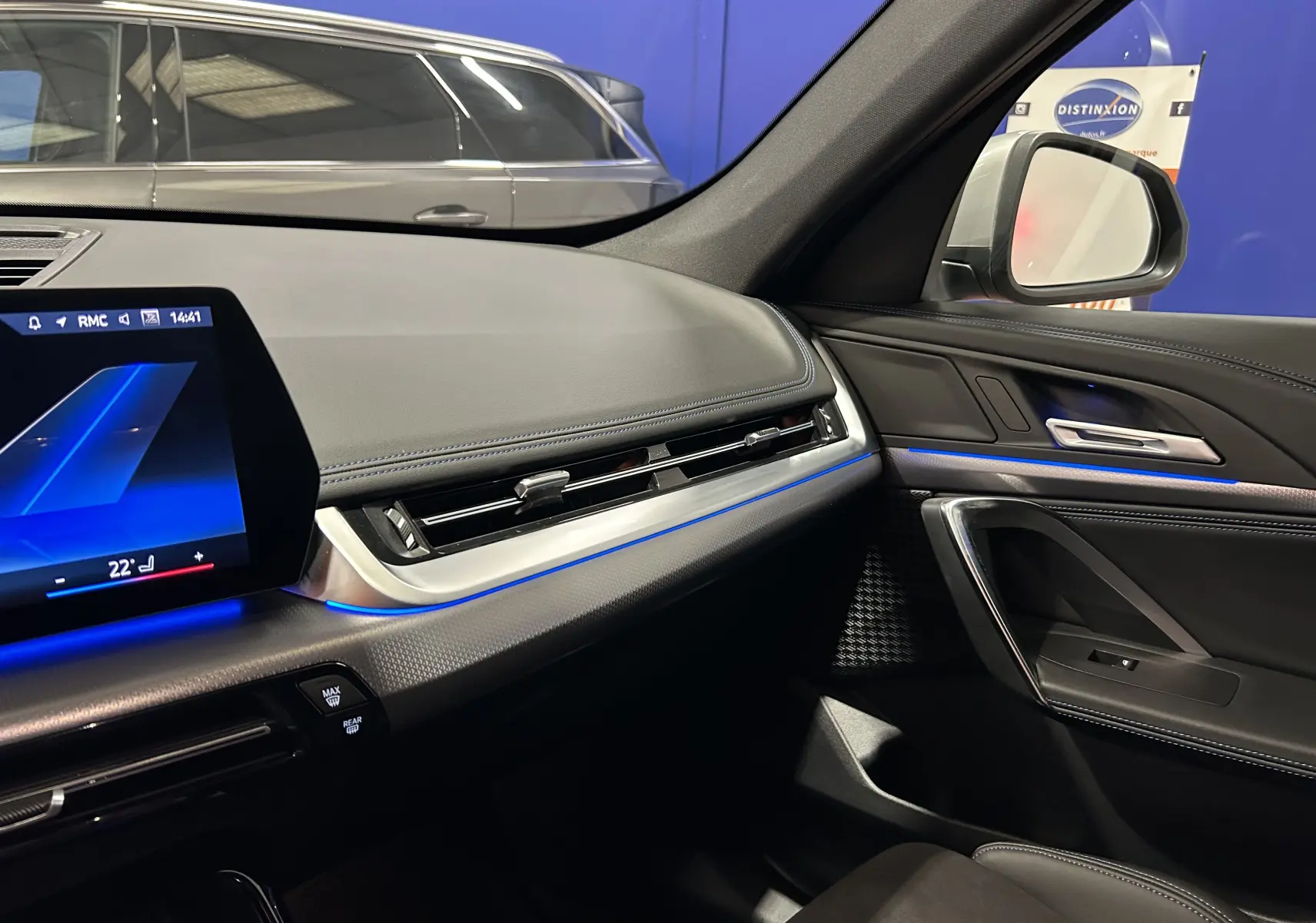 Intérieur avant droit du BMW X1 2024 Spacesilber, tableau de bord M Sport avec éclairage d'ambiance bleu et finitions cuir.