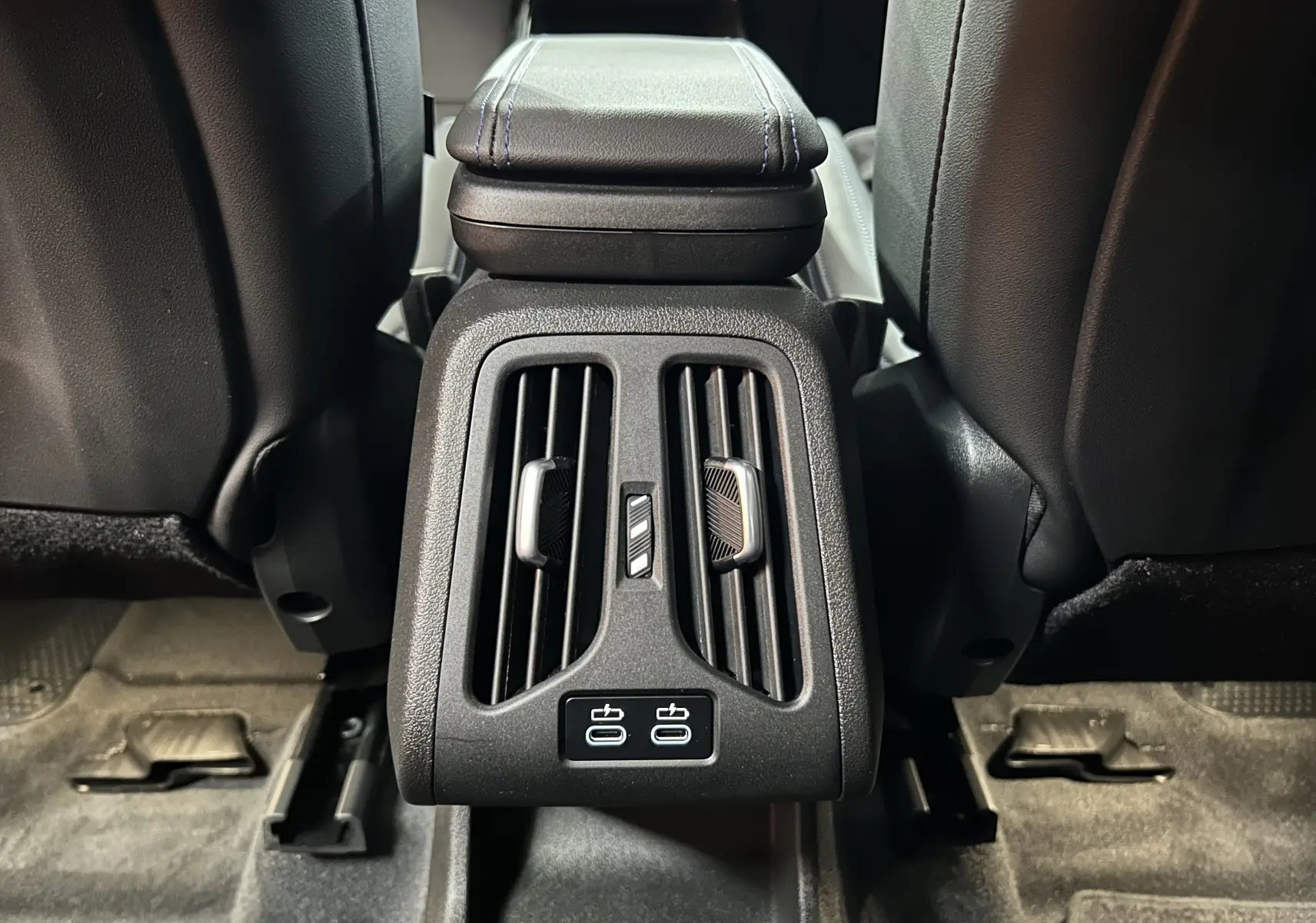 Vue rapprochée des aérateurs arrière et des ports USB sous l'accoudoir central en cuir noir du BMW X1 Spacesilber 2024.