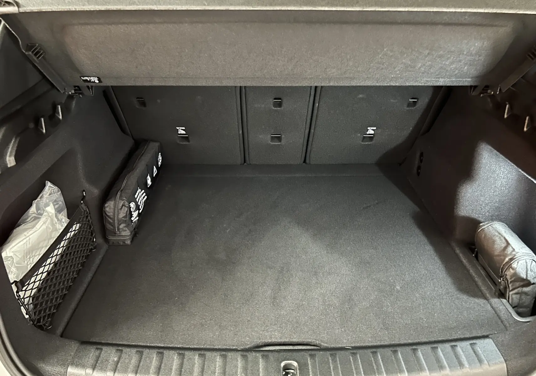 Coffre spacieux et propre d'un BMW X1 2024, vue intérieure arrière, avec rangement latéral et tapis noir.