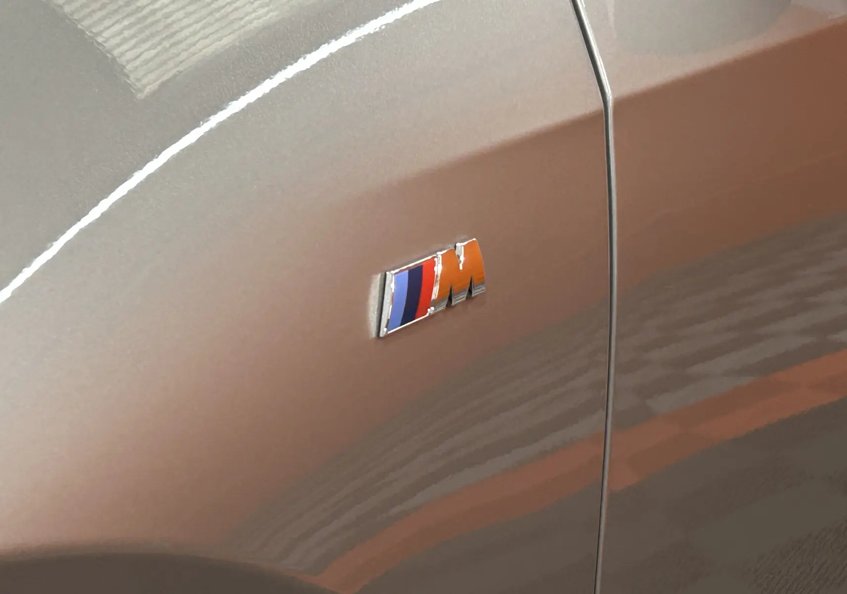 Gros plan sur l'emblème M sur la carrosserie gris spacesilber d'un BMW X1 2024 côté avant droit.