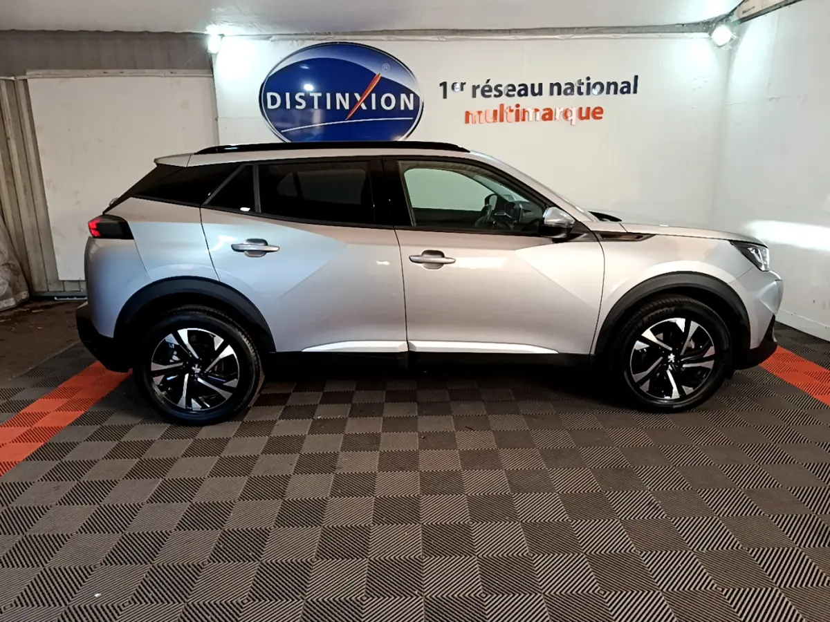 Peugeot 2008 gris clair vue de profil côté gauche dans un showroom avec jantes noires et toit panoramique.