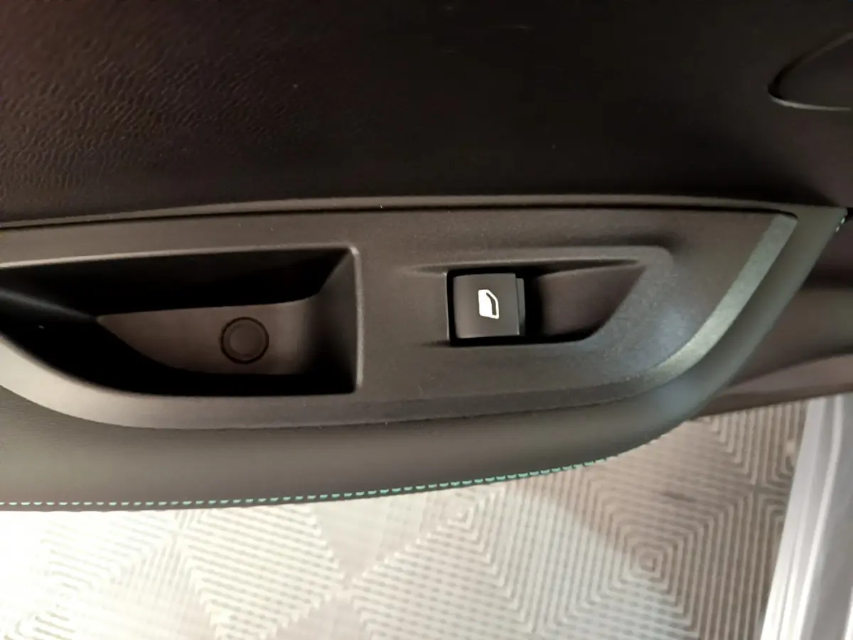 Gros plan sur le bouton d’ouverture de trappe à carburant dans l’habitacle du Peugeot 2008 gris clair, côté conducteur.