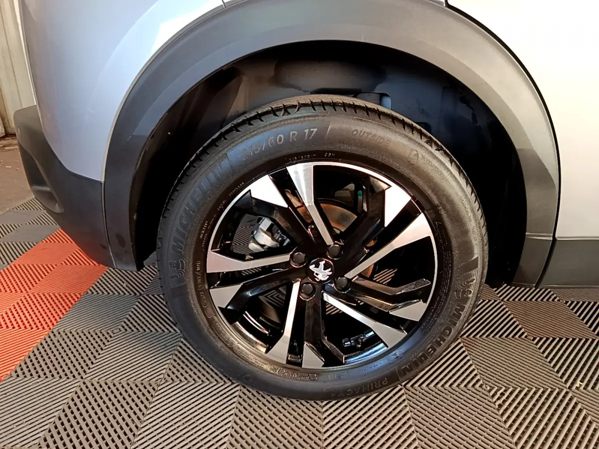 Gros plan sur la roue avant droite du Peugeot 2008 gris clair, mettant en valeur la jante noire et argentée.