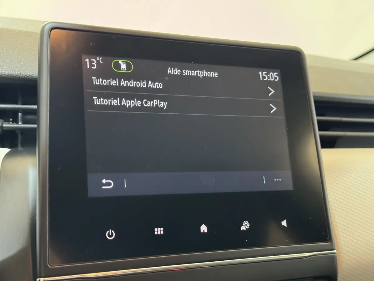 Écran tactile central du tableau de bord de la Renault Clio Business blanc, affichant tutoriels Android Auto et Apple CarPlay.