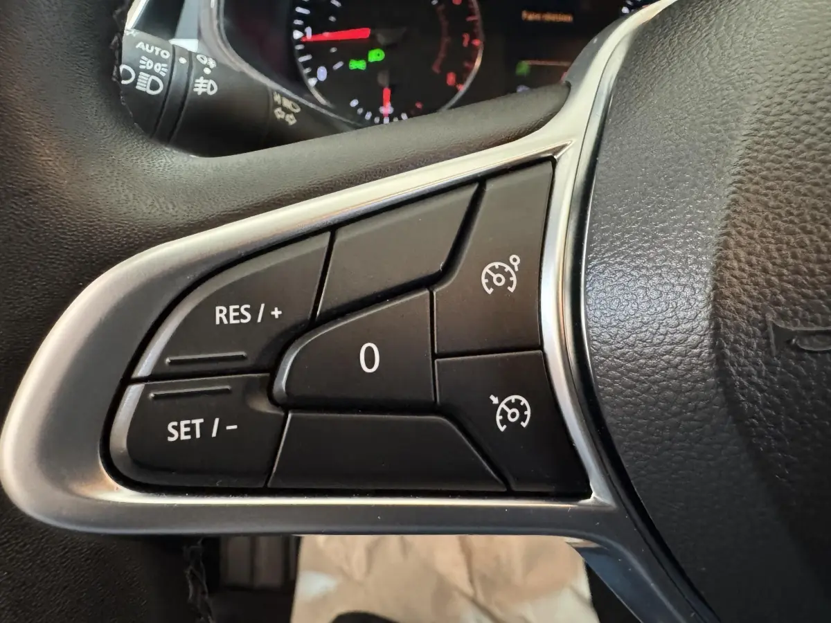 Gros plan sur les commandes de régulateur de vitesse au volant cuir noir de la Renault Clio Business TCe 100 GPL 2023.
